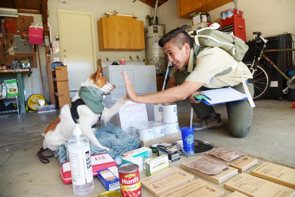 Flood Ready Freddy in garage with emergency materials laid out on the floor, giving high-five to medium sized white and brown dog