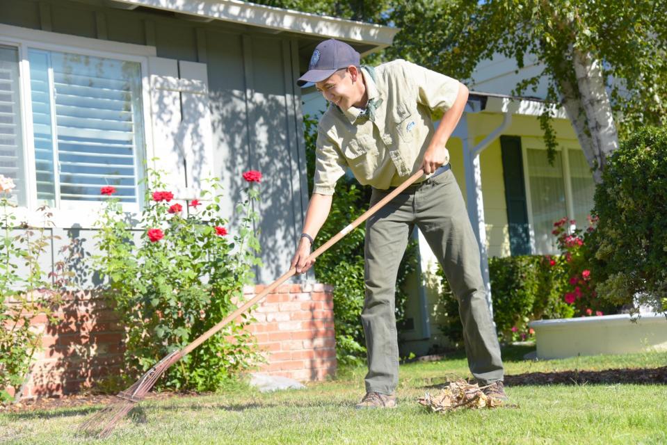 Flood Ready Freddy raking leaves away from the exterior wall of a home on a sunny day