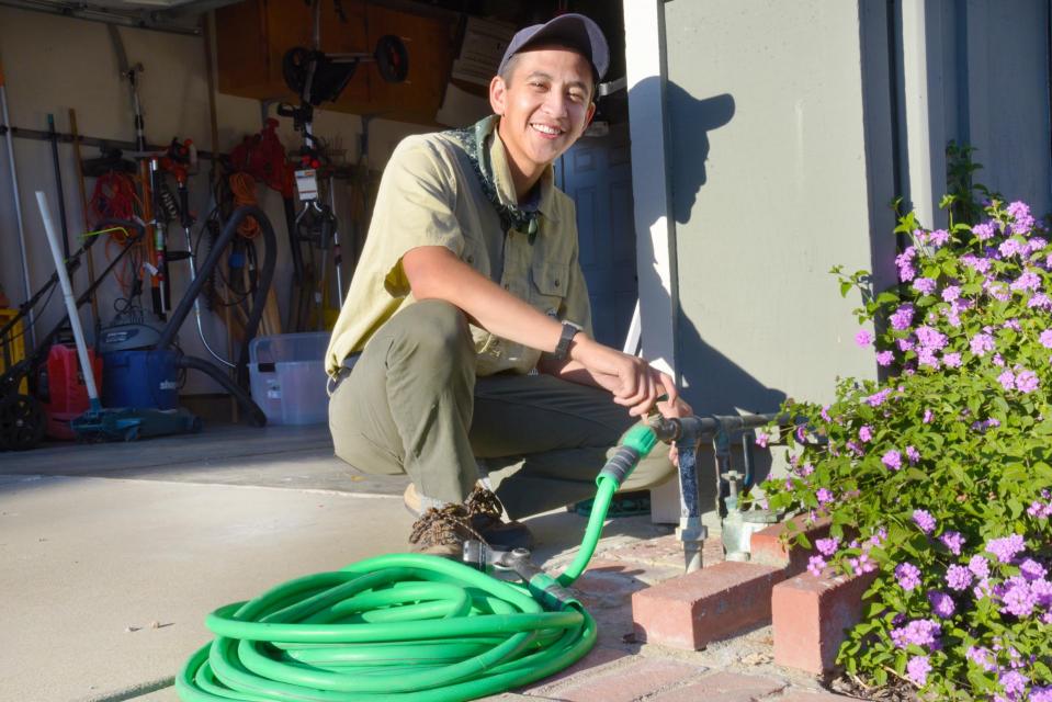 Flood Ready Freddy smiling and kneeling by wrapped up garden hose next to open garage door