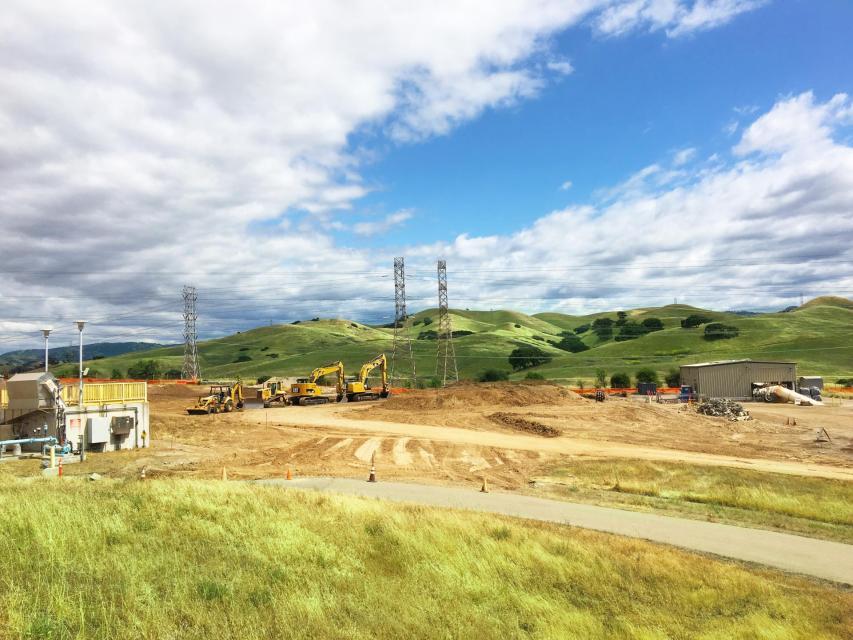 Sunny construction site surrounded by grassy hills.