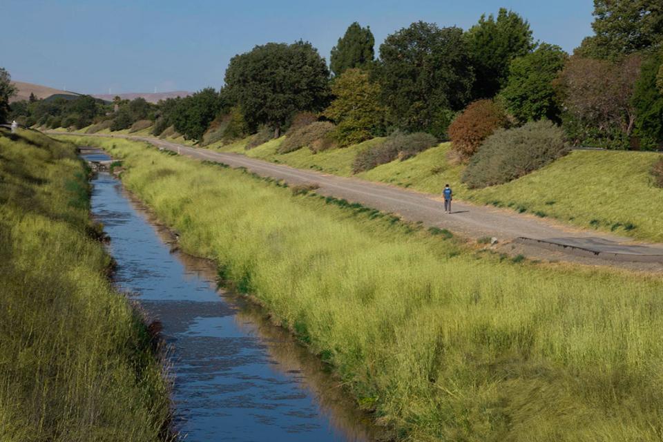 A blue stream alongside a trail in between two grassy banks