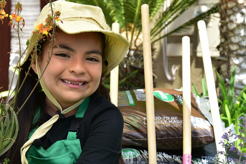 Smiling child holding holding a potted plant in a garden